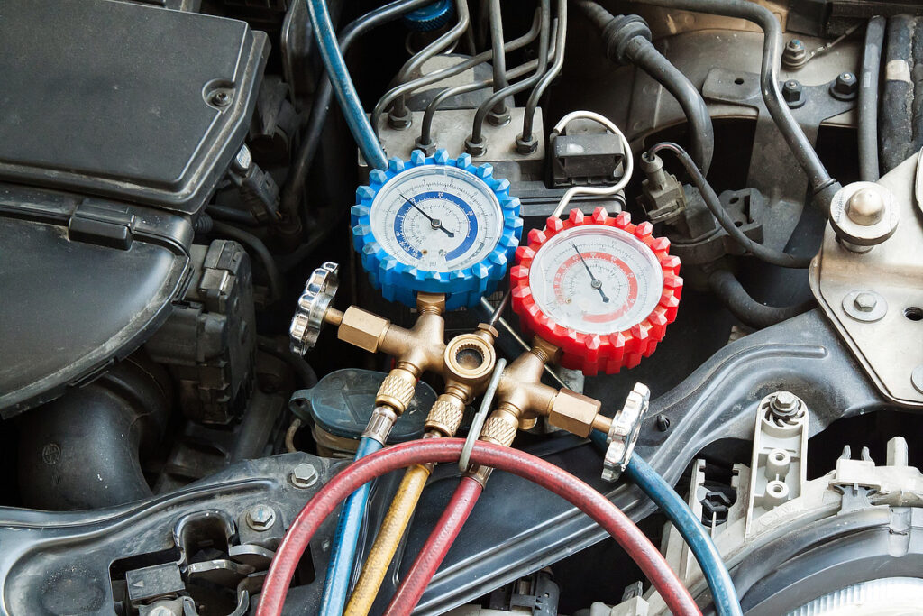 Nahaufnahme eines Automotors mit angeschlossenen blauen und roten Druckmessgeräten, die Messwerte für eine MFK-Inspektion bei Frey Auto AG anzeigen. Frey Auto AG ist auf Fahrzeuge der Marken Toyota, Lexus und Suzuki spezialisiert und bietet fachmännischen Reifenservice, umfassende Fahrzeugwartung, Karosseriereparaturen und professionelle Autowaschlösungen, um Spitzenleistung und Langlebigkeit Ihres Fahrzeugs sicherzustellen.