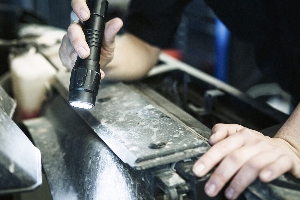 Mit einer Taschenlampe nimmt ein Techniker Autoteile bei der Frey Auto AG unter die Lupe. Die Werkstatt ist spezialisiert auf MFK-Inspektionen, Reifenservice und umfassenden Autoservice. Die Werkstatt betreut die renommierten Automarken Toyota, Lexus und Suzuki.
