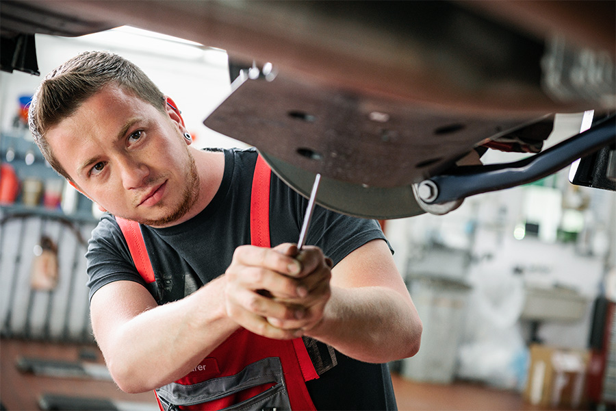 Ein gelernter Mechaniker in einer roten Schürze bedient sich in der Werkstatt der Frey Auto AG fachmännisch eines Schraubenziehers an einem Toyota-Fahrzeugteil. Das Unternehmen ist auf MFK-Inspektionen, Reifendienste, umfassenden Autoservice und präzise Karosseriearbeiten spezialisiert und bietet eine erstklassige Auswahl an Toyota-, Lexus- und Suzuki-Autos zum Verkauf an.