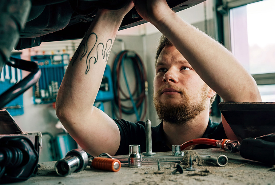 Ein Kfz-Mechaniker mit einem tätowierten Arm, der bei der Frey Auto AG Wartungsarbeiten an Fahrzeugen der Marken Toyota, Lexus oder Suzuki durchführt, darunter Dienstleistungen wie die MFK-Prüfung, Reifenservice und allgemeine Karosseriearbeiten.