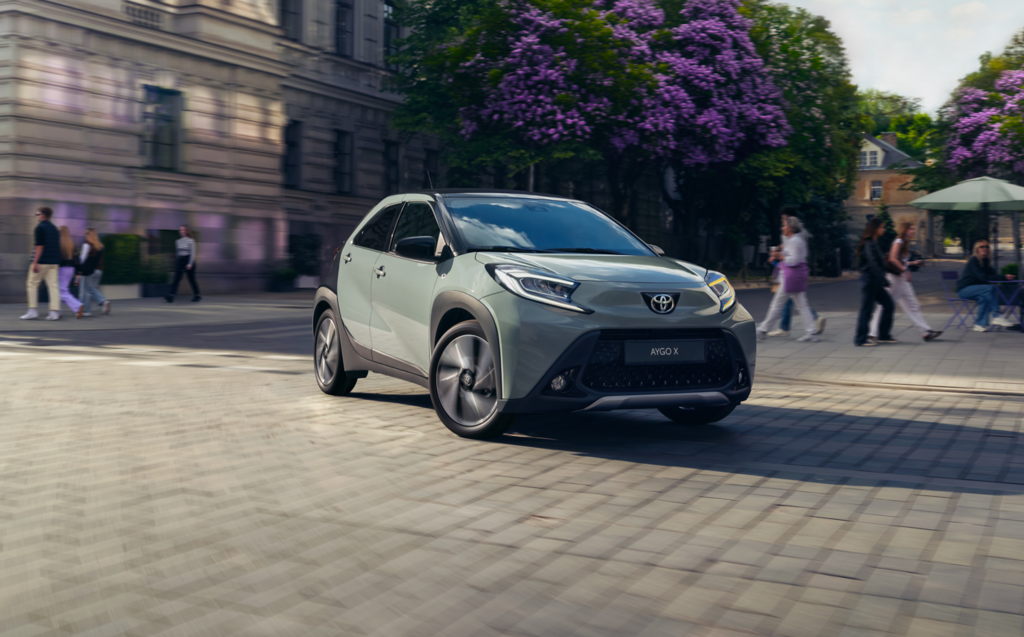 Ein grauer Toyota SUV navigiert durch eine Kopfsteinpflasterstraße voller Fußgänger und Café-Tische im Freien vor der Kulisse eines historischen Gebäudes und blühender Bäume. Frey Auto AG bietet umfassende Dienstleistungen an, darunter MFK-Inspektionen, Reifenservice, Karosseriearbeiten und Autoverkauf für führende Marken wie Toyota, Lexus und Suzuki. Unsere detaillierten Autowaschdienste sorgen dafür, dass Ihr Fahrzeug seinen makellosen Zustand behält.
