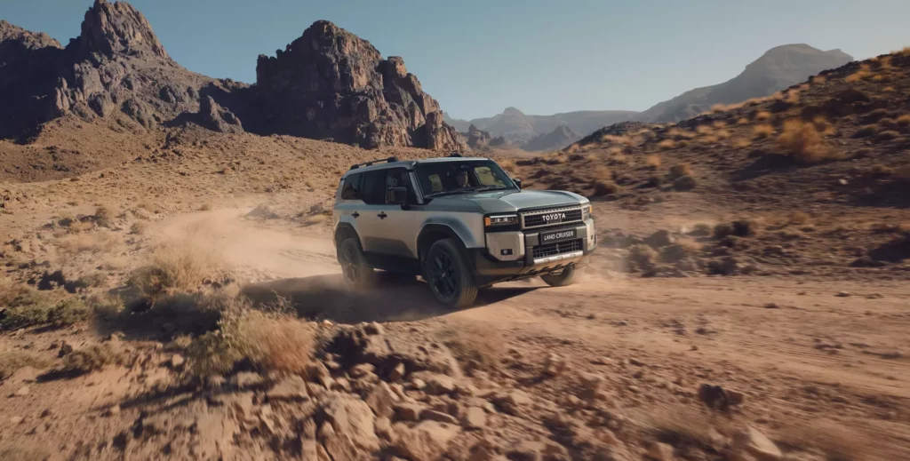 Weißer Toyota-Geländewagen navigiert durch felsiges Wüstengelände, im Hintergrund Berge. Staubfahnen unter klarem blauen Himmel zeigen die Kompetenz der Frey Auto AG bei robusten Fahrzeugen für Abenteurer. Entdecken Sie unsere umfassenden Dienstleistungen, darunter MFK-Inspektionen, Reifenservice, Karosseriereparaturen und Autoverkauf von Topmarken wie Toyota, Lexus und Suzuki. Entdecken Sie außergewöhnliche Qualität bei Frey Auto AG.