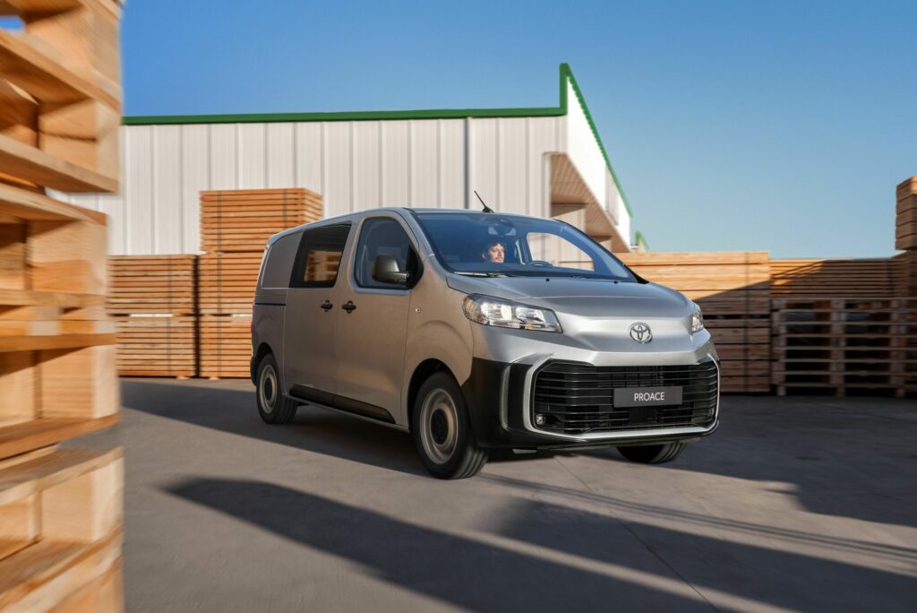 Ein silberner Toyota-Transporter fährt an einem sonnigen Tag zwischen Stapeln von Holzpaletten in der Nähe eines Lagerhauses und symbolisiert die umfassenden Kfz-Dienstleistungen der Frey Auto AG. Das Unternehmen ist auf Marken wie Toyota, Lexus und Suzuki spezialisiert und bietet fachmännische MFK-Inspektionen, Reifenservice, routinemäßige Wartungskontrollen, präzise Karosseriereparaturen und einen umfassenden Neu- und Gebrauchtwagenverkauf. Das Unternehmen bietet auch gründliche Autowaschoptionen an, um sicherzustellen, dass alle Fahrzeuge ihre Obhut in makellosem Zustand verlassen.