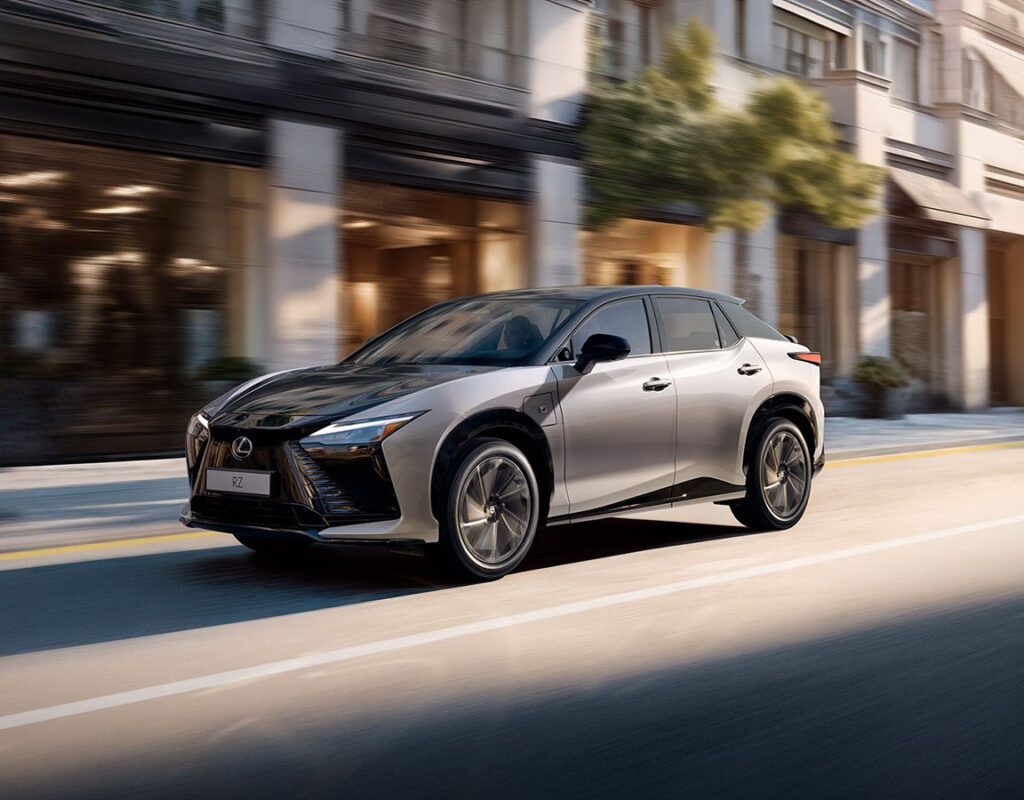 Ein silberner Lexus RZ Elektro-SUV von Frey Auto AG fährt eine Stadtstraße entlang und steht symbolisch für unsere Kompetenz im professionellen Autoverkauf und im Kfz-Service.