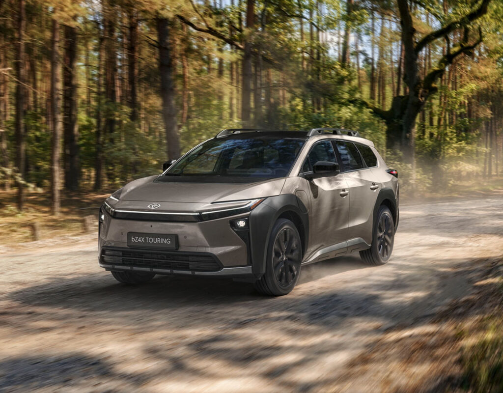 Ein Toyota bZ4X Touring auf einer unbefestigten Straße durch den Wald – erhältlich bei der Frey Auto AG, die Autoverkauf, professionellen Service und fachmännische Karosseriearbeiten anbietet.