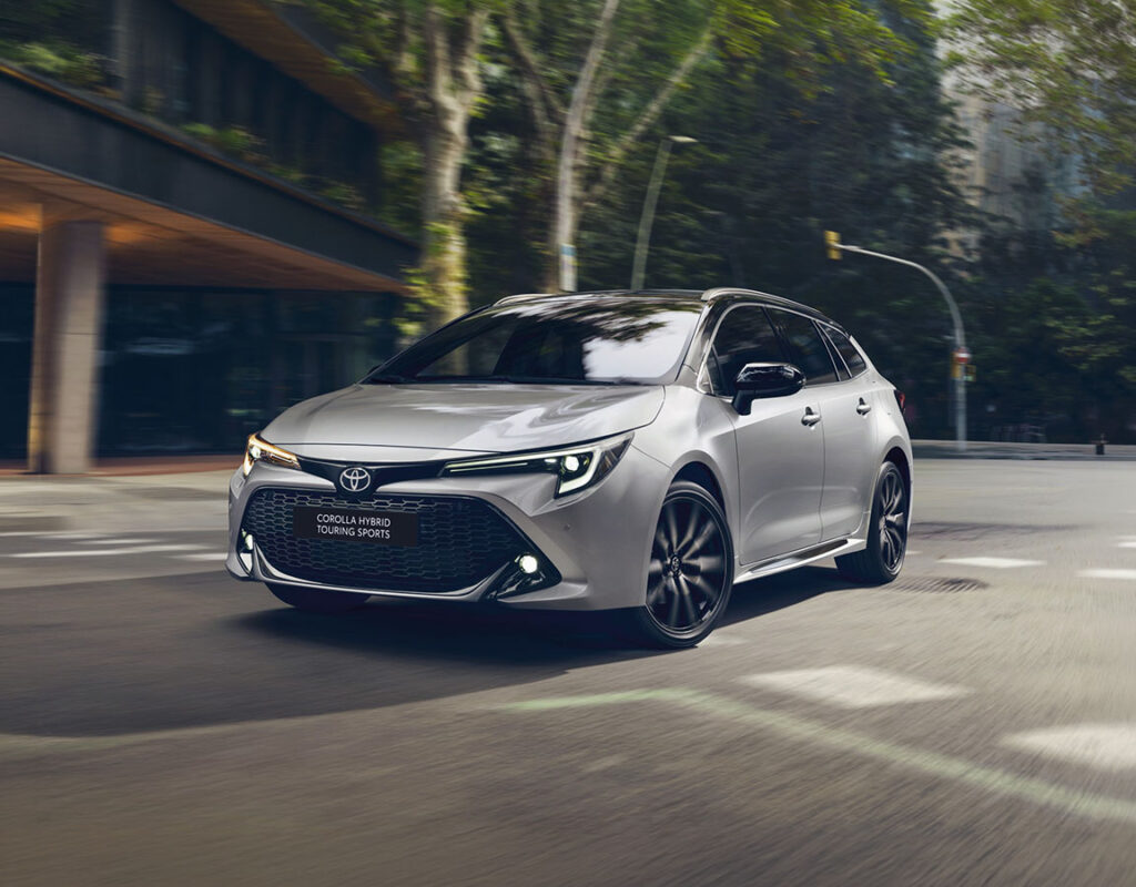 Ein silberner Toyota Corolla Hybrid Touring Sports fährt auf einer Stadtstraße und steht symbolisch für den zuverlässigen Autoverkauf und das umfassende Serviceangebot der Frey Auto AG, darunter MFK-Prüfung, Reifenservice, Karosseriearbeiten und Autowäsche für Fahrzeuge der Marken Toyota, Lexus und Suzuki.