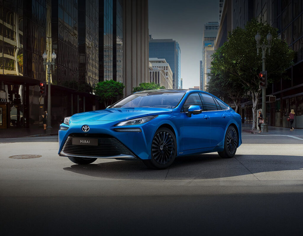 Ein blauer Toyota Mirai von Frey Auto AG, der zum Verkauf steht, steht auf einer Straße in der Stadt.