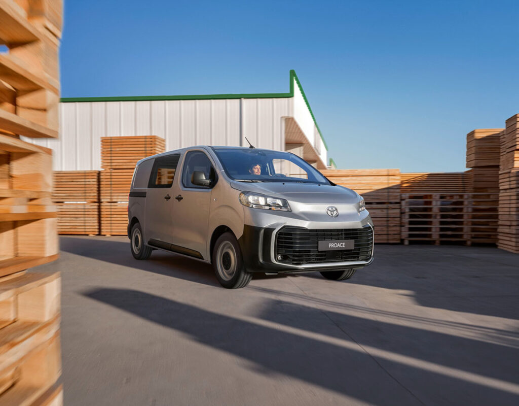 Ein silberner Toyota Proace-Nutzfahrzeug der Frey Auto AG fährt durch einen Lagerhof und symbolisiert unsere professionellen Kfz-Dienstleistungen, darunter den Verkauf von Toyota-Fahrzeugen, Karosseriearbeiten und fachgerechte Wartung.