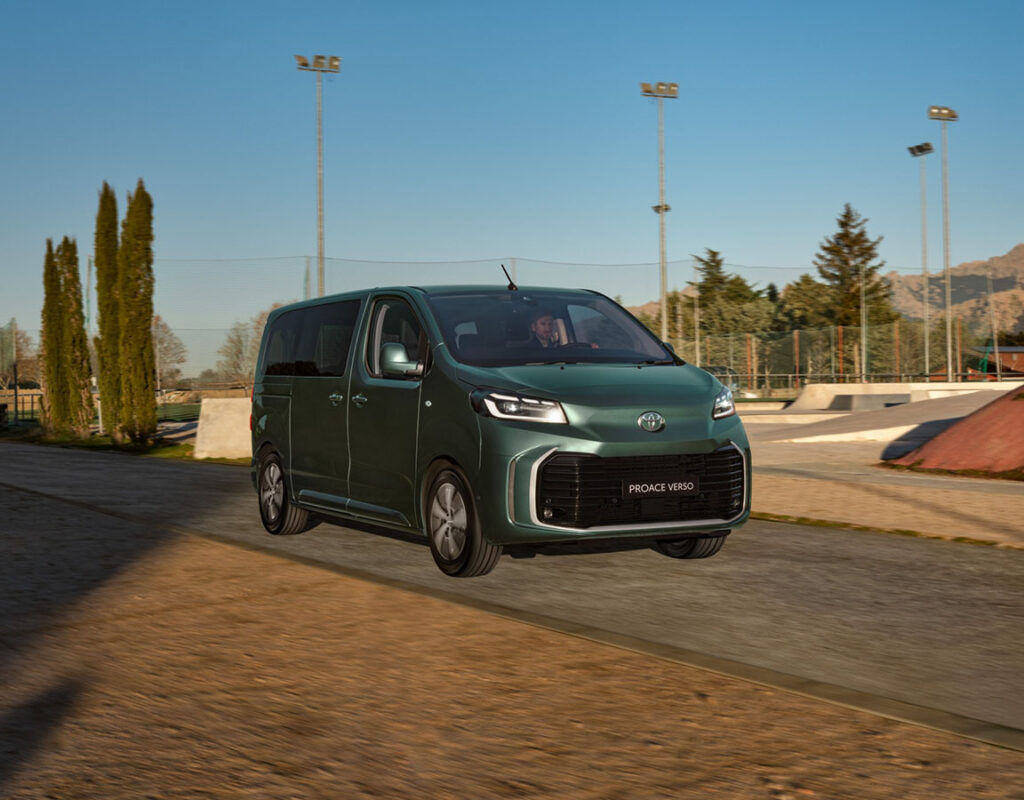 Ein grüner Toyota Proace Verso, der bei der Frey Auto AG zum Verkauf und für professionellen Service angeboten wird, fährt auf einer asphaltierten Straße in der Nähe eines Skateparks.